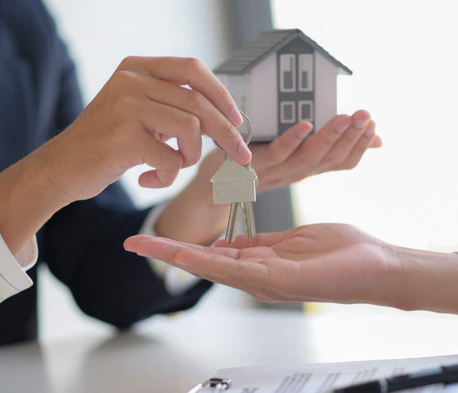 Two people holding a small house model together, showcasing teamwork and excitement for their new home.