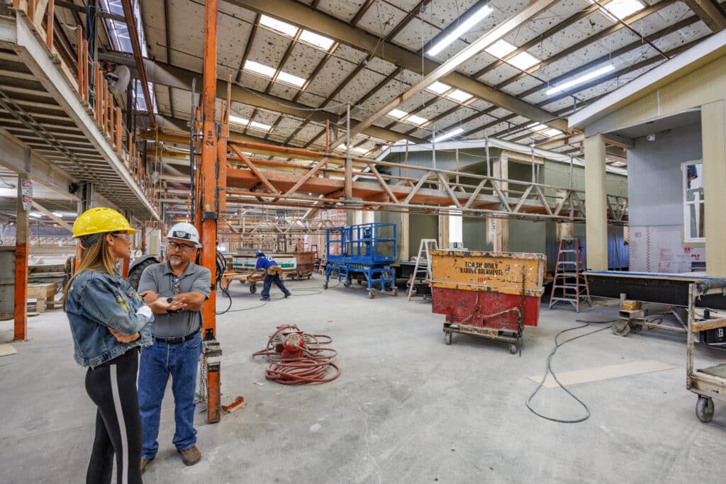 A large warehouse filled with construction gear, featuring two people standing and discussing nearby.