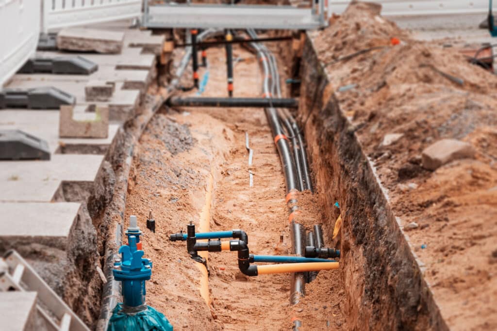 A pipe is being placed underground next to a house, indicating ongoing construction or utility installation.